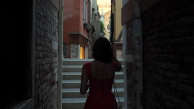 Kırmızı yaz elbiseli turist Venedik 'in arka sokağına bakıyor.