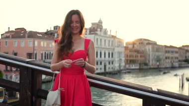 Büyük Kanal İtalya üzerindeki köprüde kırmızı elbiseli, gülümseyen kadın turist.