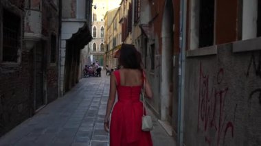 Kırmızı yaz elbiseli turist Venedik sokaklarında binalarla geziniyor.