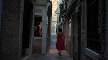 Kırmızı yaz elbiseli turist Venedik caddesinde yansımalarla geziniyor.