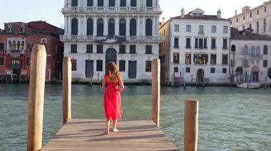 Kırmızı elbiseli kadın Venedik mimarisi ile rıhtımda.