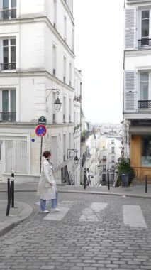 Montmartre Paris 'te kaldırım taşı caddesinde yürüyen açık renk ceketli genç bir kadın. 