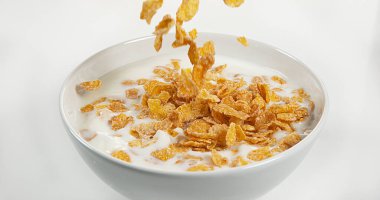 Mısır gevrekleri beyaz arkaplana karşı bir süt kasesine düşüyor