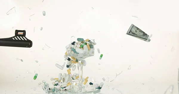 Glass filled with Capsules and Dollars Exploding against White Background