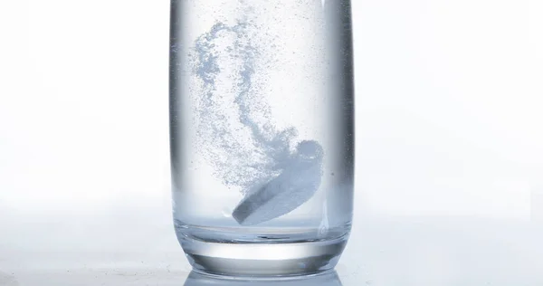 ホワイトバックグラウンドに対する水のガラスに落ちて溶解する錠剤 — ストック写真