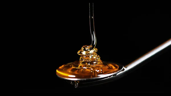 蜂蜜在黑色背景下在勺子上流动 — 图库照片