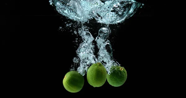 Limões Verdes Citrus Aurantifolia Frutas Caindo Água Contra Fundo Preto — Fotografia de Stock