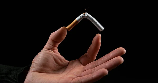 ブラックバックグラウンドでタバコを壊す男の手 — ストック写真