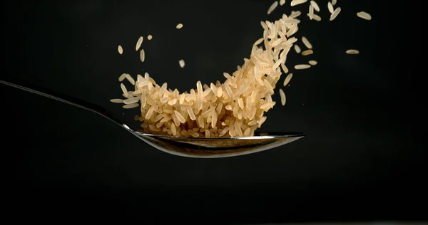 黒い背景に対してスプーンに落ちる米 — ストック写真