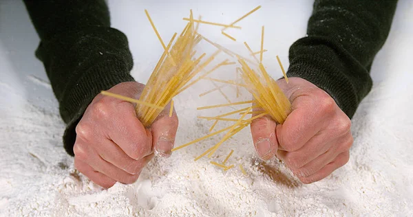 Hands of Man Breaking Spaghetti Pasta against Flour Background
