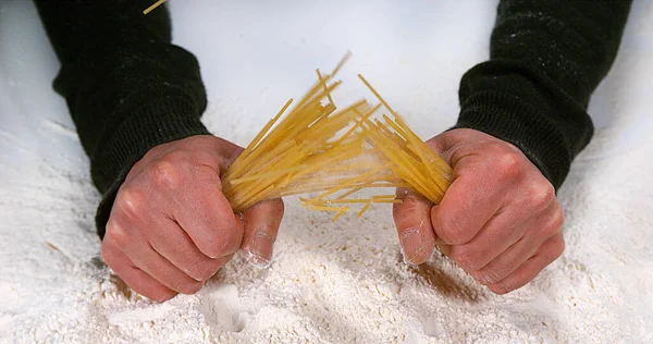 Hands of Man Breaking Spaghetti Pasta against Flour Background
