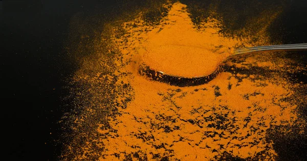 ターメリック カルクマガム ブラックバックグラウンドに対してスプーンに落ちる粉 インディアンスパイス — ストック写真