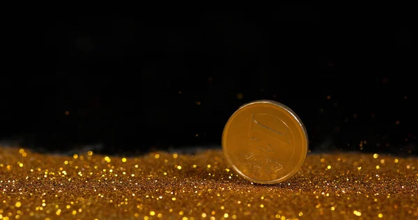 Coin of 1 Euro Rolling on Gold Powder against Black Background