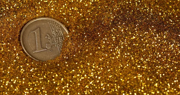 Coin of 1 Euro Rolling on Gold Powder against Black Background