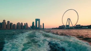 Gün batımında Ain Dubai ile Dubai ufuk çizgisi Dubai Marinaları gökdelenleri ve Ain Dubai dönme dolabı ile gökyüzü manzarası gün batımında sudan yakalanmıştır..