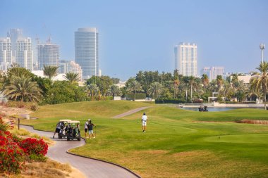 Dubai 'de City Skyline ile lüks golf sahası, yemyeşil bir saha üzerinde Golfçüler palmiye ağaçları, golf arabaları ve Dubai' de berrak bir gökdelenle çevrili modern gökdelenler..  