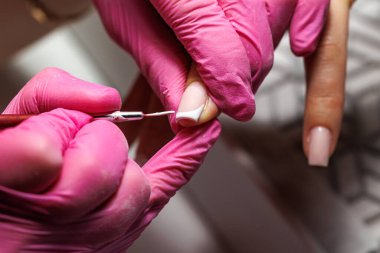 Manikür prosedürü sırasında, pembe eldivenli bir güzellik uzmanının müşterinin eline tırnak etlerini iterken yakın plan görüntüsü, Fransız tırnakları. Yüksek kalite fotoğraf