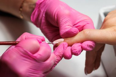 Manikür prosedürü sırasında, pembe eldivenli bir güzellik uzmanının müşterinin eline tırnak etlerini iterken yakın plan görüntüsü, Fransız tırnakları. Yüksek kalite fotoğraf