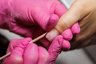 Manikür için manikür yapan bir tırnak teknisyeninin yakın çekimi. Tahta bir sopayla, pembe eldivenler giyerek.. 