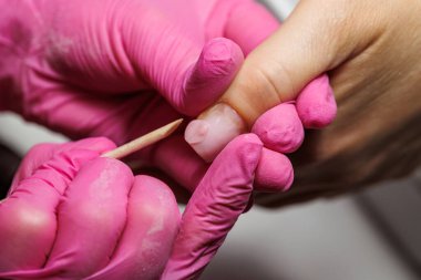 Manikür için manikür yapan bir tırnak teknisyeninin yakın çekimi. Tahta bir sopayla, pembe eldivenler giyerek.. 