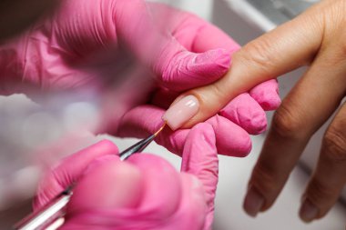 Manikür prosedürü sırasında, pembe eldivenli bir güzellik uzmanının müşterinin eline tırnak etlerini iterken yakın plan görüntüsü, Fransız tırnakları. Yüksek kalite fotoğraf