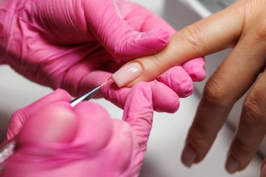 Manikür prosedürü sırasında, pembe eldivenli bir güzellik uzmanının müşterinin eline tırnak etlerini iterken yakın plan görüntüsü, Fransız tırnakları. Yüksek kalite fotoğraf