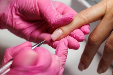 Manikür prosedürü sırasında, pembe eldivenli bir güzellik uzmanının müşterinin eline tırnak etlerini iterken yakın plan görüntüsü, Fransız tırnakları. Yüksek kalite fotoğraf