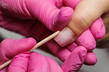 Manikür için manikür yapan bir tırnak teknisyeninin yakın çekimi. Tahta bir sopayla, pembe eldivenler giyerek.. 
