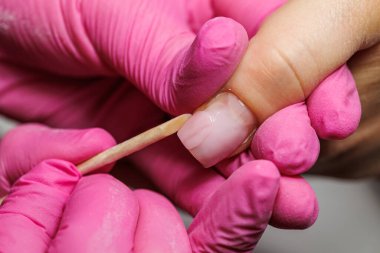 Manikür için manikür yapan bir tırnak teknisyeninin yakın çekimi. Tahta bir sopayla, pembe eldivenler giyerek.. 
