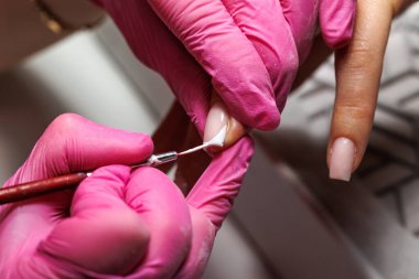 Manikür prosedürü sırasında, pembe eldivenli bir güzellik uzmanının müşterinin eline tırnak etlerini iterken yakın plan görüntüsü, Fransız tırnakları. Yüksek kalite fotoğraf