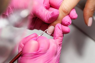 Manikür prosedürü sırasında, pembe eldivenli bir güzellik uzmanının müşterinin eline tırnak etlerini iterken yakın plan görüntüsü, Fransız tırnakları. Yüksek kalite fotoğraf