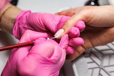 Manikür prosedürü sırasında, pembe eldivenli bir güzellik uzmanının müşterinin eline tırnak etlerini iterken yakın plan görüntüsü, Fransız tırnakları. Yüksek kalite fotoğraf