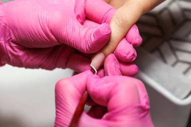 Manikür prosedürü sırasında, pembe eldivenli bir güzellik uzmanının müşterinin eline tırnak etlerini iterken yakın plan görüntüsü, Fransız tırnakları. Yüksek kalite fotoğraf