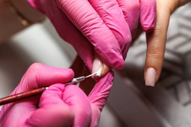 Manikür prosedürü sırasında, pembe eldivenli bir güzellik uzmanının müşterinin eline tırnak etlerini iterken yakın plan görüntüsü, Fransız tırnakları. Yüksek kalite fotoğraf