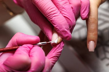 Manikür prosedürü sırasında, pembe eldivenli bir güzellik uzmanının müşterinin eline tırnak etlerini iterken yakın plan görüntüsü, Fransız tırnakları. Yüksek kalite fotoğraf