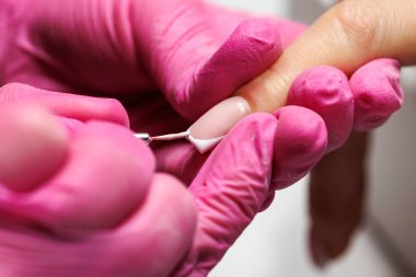 Manikür prosedürü sırasında, pembe eldivenli bir güzellik uzmanının müşterinin eline tırnak etlerini iterken yakın plan görüntüsü, Fransız tırnakları. Yüksek kalite fotoğraf