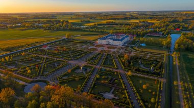 Gün batımında simetrik Fransız tarzı bahçeler ve gür kırsal bölgelerle çevrili zarif bir Barok tarzı sarayın insansız hava aracı fotoğrafı. Çalışma Sarayı 