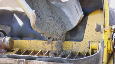 Concrete Pouring from Mixer Truck into Hopper, Close-up video of wet concrete being poured from a mixer truck chute into the hopper of a construction machine