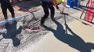 Video of a construction worker in rubber boots pouring concrete over red underfloor heating pipes during a foundation installation. High quality 4k footage