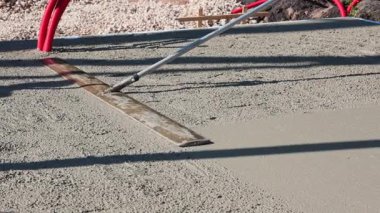 Bir inşaat işçisinin yeni dökülmüş beton zemini düzleştirmek ve düzleştirmek için uzun kulplu bir mala kullandığı yakın çekim görüntüleri. Yüksek kalite 4k görüntü