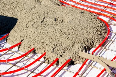 Çelik bir ağ örgüsüne bağlı kırmızı yeraltı ısıtma boruları inşaat alanına yeni dökülmüş betonla kaplanıyor. Yüksek kalite fotoğraf