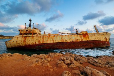 Terk edilmiş paslı gemi enkazı gün batımında sarp kayalıklarda dinleniyor, dramatik gökyüzünün altında Kıbrıs kıyıları yakınlarında yakalandı.. 