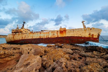Terk edilmiş paslı gemi enkazı gün batımında sarp kayalıklarda dinleniyor, dramatik gökyüzünün altında Kıbrıs kıyıları yakınlarında yakalandı.. 