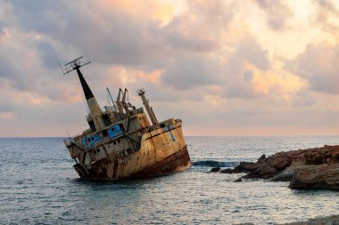 Terk edilmiş paslı gemi enkazı gün batımında sarp kayalıklarda dinleniyor, dramatik gökyüzünün altında Kıbrıs kıyıları yakınlarında yakalandı.. 