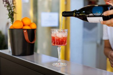 Barmen bardağa kırmızı kokteyl dökerken, barmenin bardağa buz küpleriyle parlak kırmızı kokteyl dökerken, bardakları karıştırırken, içkileri tazelerken, bardakları tazelerken.