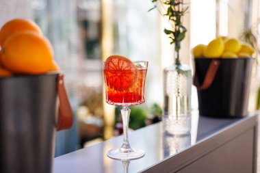 Klasik Negroni kokteyli, kristal bardakta portakal dilimi ile servis edilir, doğal ışıkta şık bir bar tezgahına yerleştirilir. Yüksek kalite fotoğraf