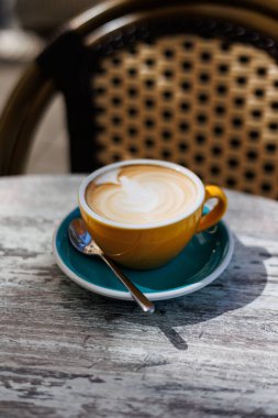 Açık bir kafede kaşıkla turkuaz bir fincan üzerinde servis edilen kremalı latte ile taze yapılmış kapuçino. Yüksek kalite fotoğraf.