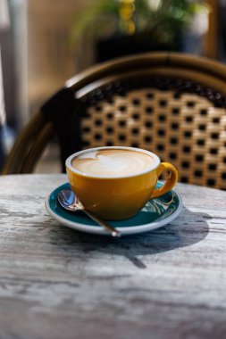 Açık bir kafede kaşıkla turkuaz bir fincan üzerinde servis edilen kremalı latte ile taze yapılmış kapuçino. Yüksek kalite fotoğraf.