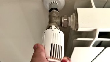 Bir kadının eli radyatörün ısıtma düğmesini, bataryasını çevirir. Evdeki ısıtma sistemi. Elektrikli radyatör. Isıtma cihazları. Kışın ve sonbaharda evin ısıtması. Sıcak bir ev. 4K
