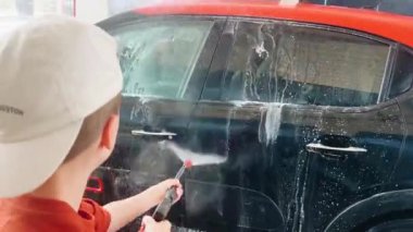 Genç çocuk oto yıkamada araba hortumluyor. 4K 'lık yüksek kaliteli görüntüler.
